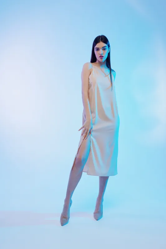 Elegant woman in a beige satin dress poses confidently in a studio with blue lighting. Concept for beauty, fashion, style, and modern elegance.