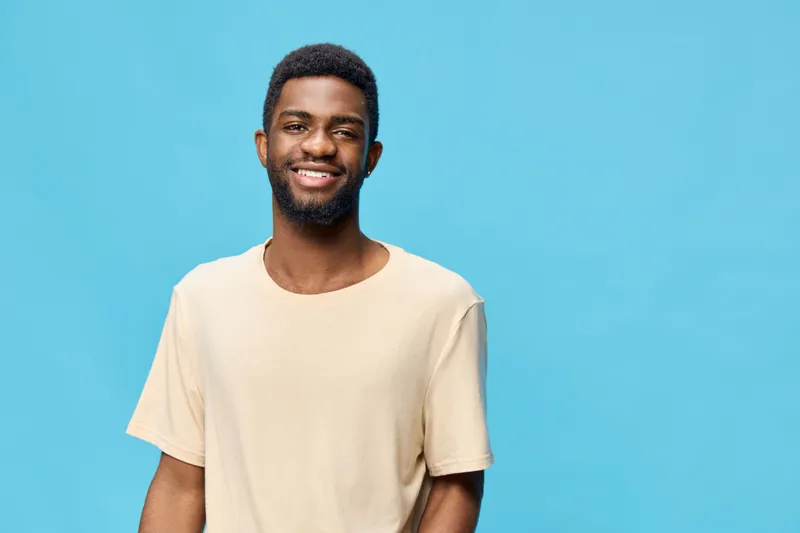 Cheerful African American man in a beige shirt smiling against a bright blue background, capturing a sense of joy and positivity, ideal for lifestyle concepts