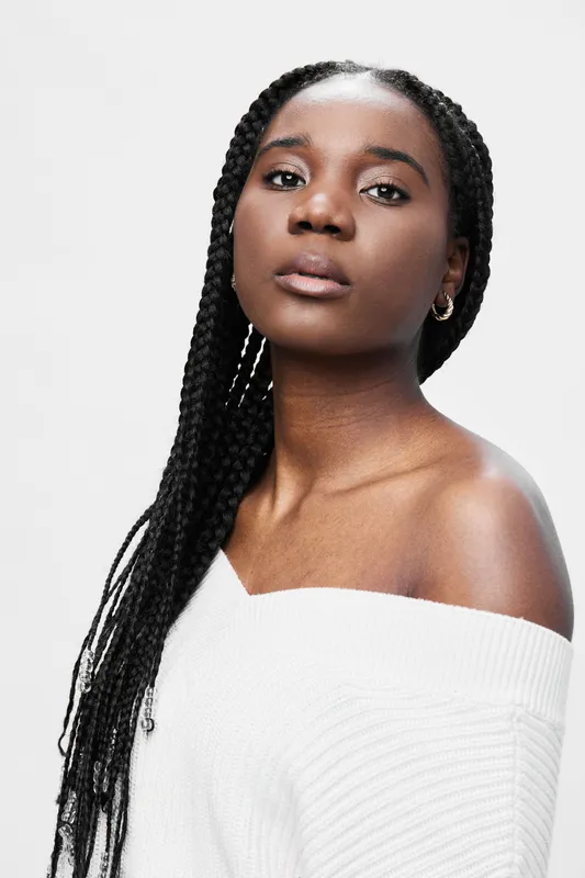 Portrait of a confident Black woman with braids wearing a stylish white off shoulder sweater, showcasing beauty and self expression against a neutral background