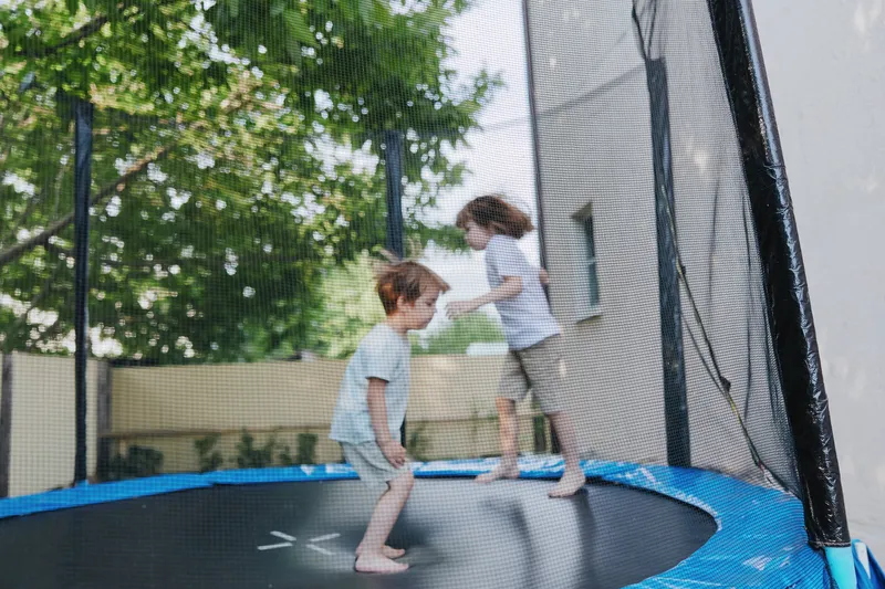 Happy children jumping on a trampoline in a sunny backyard, enjoying their playful moment surrounded by greenery and fresh air.