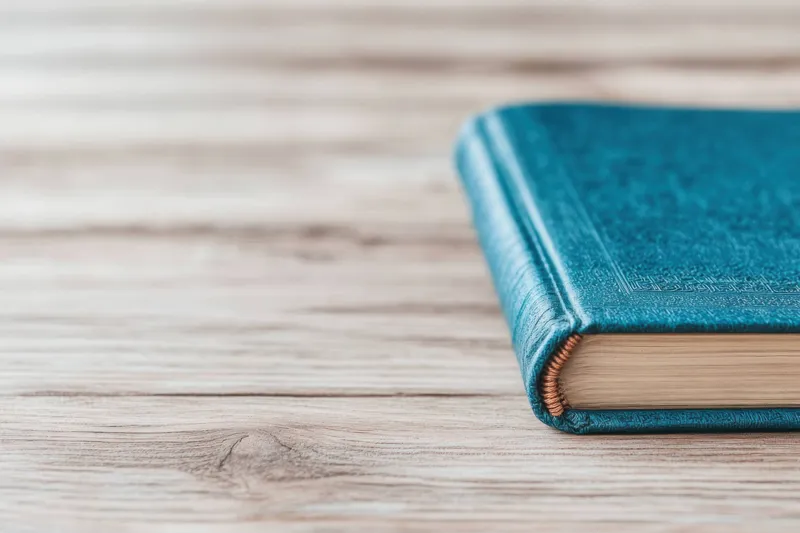 Детальный снимок книги в бирюзовом твёрдом переплёте на деревянной поверхности, передающий ощущение знаний и творчества
