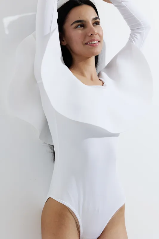 woman sport fitness wearing white activewear stretching arms indoors with soft natural light and modern minimalist background in fitness concept