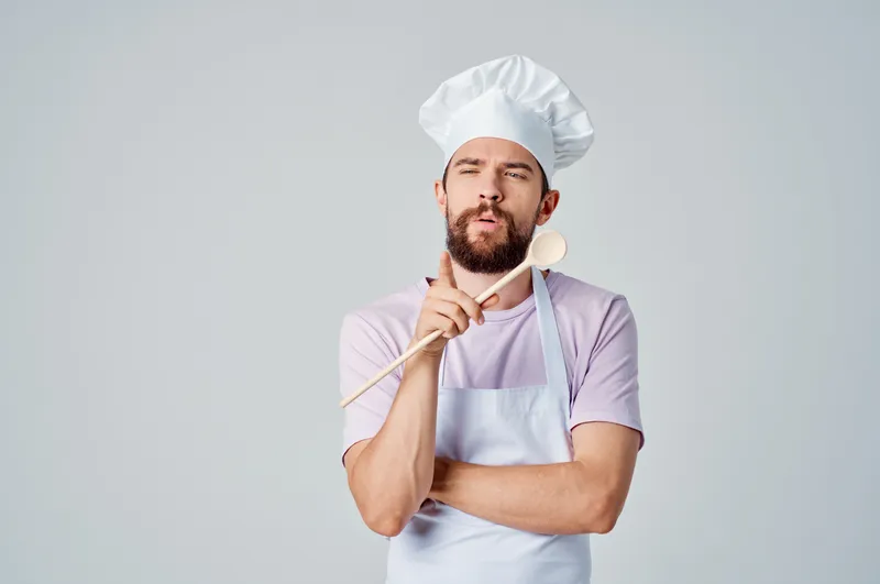 Шеф-повар с деревянной ложкой в руке работает на профессиональной кухне