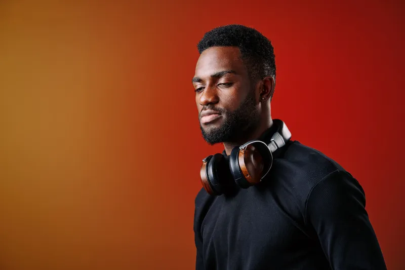 Calm young African American man with headphones enjoying music against a vibrant orange background, conveying peace and relaxation