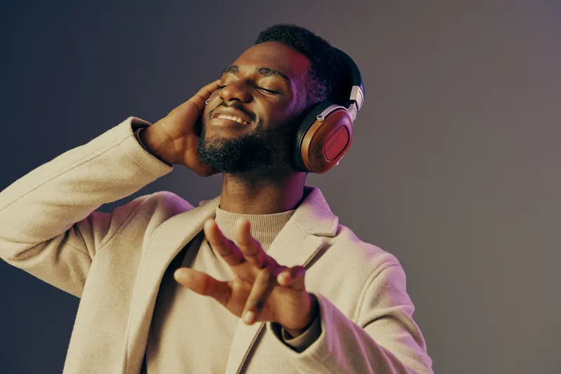 Smiling African American man enjoying music with headphones in a stylish casual outfit against a gradient background, embodying happiness and relaxation