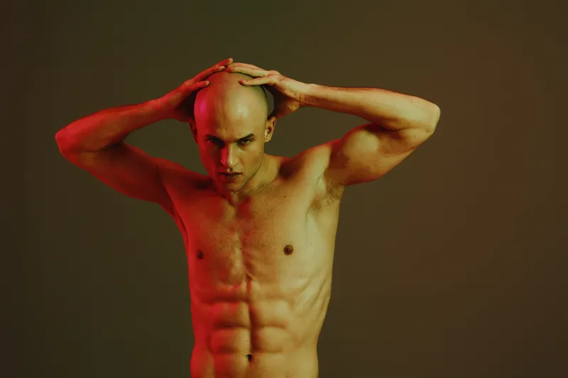 Strong man with an athletic build poses dramatically, conveying intensity and inner strength against a dark, moody background with dramatic lighting.