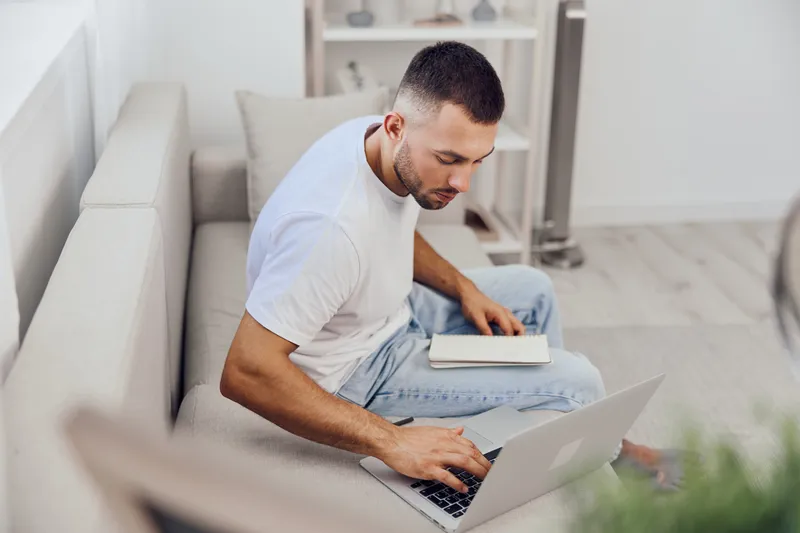 Focused man working on a laptop at home, casual attire, modern interior, bright lighting. Perfect for showcasing remote work lifestyle trends of 2025.