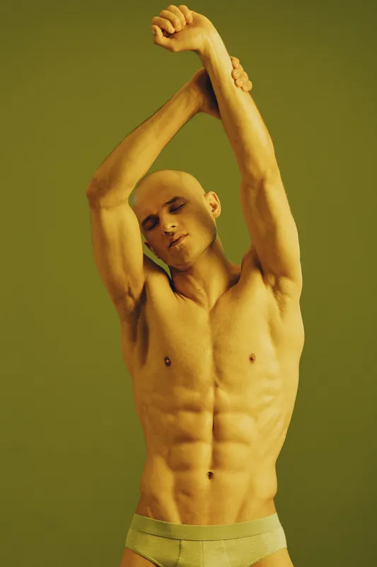 Athletic man stretching with a calm expression, showcasing toned muscles. The unique lighting highlights his physique in a vibrant hue.