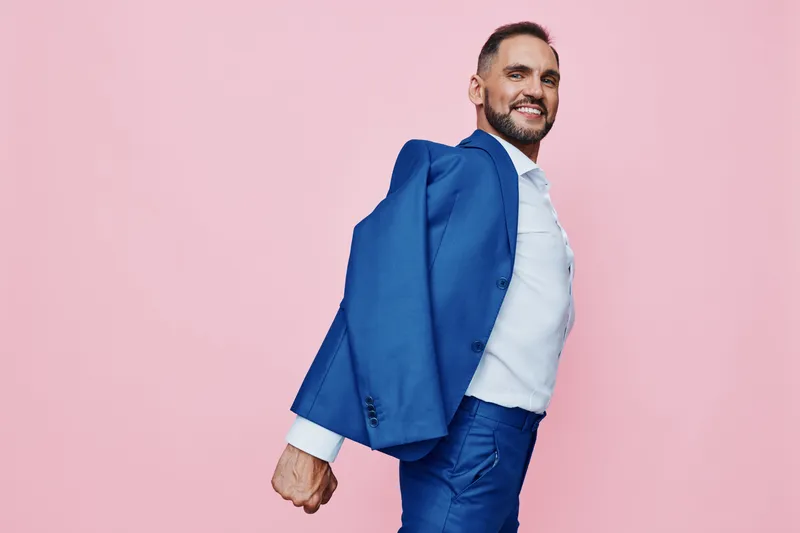 A confident professional man in a blue suit bursts with joy against a vibrant pink background, creating a dynamic, isolated color setting that highlights his upbeat mood.
