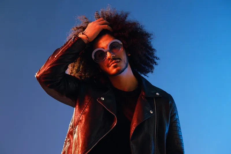 Портрет стильного мужчины с кудрявыми волосами, в очках, с улыбкой на синем фоне