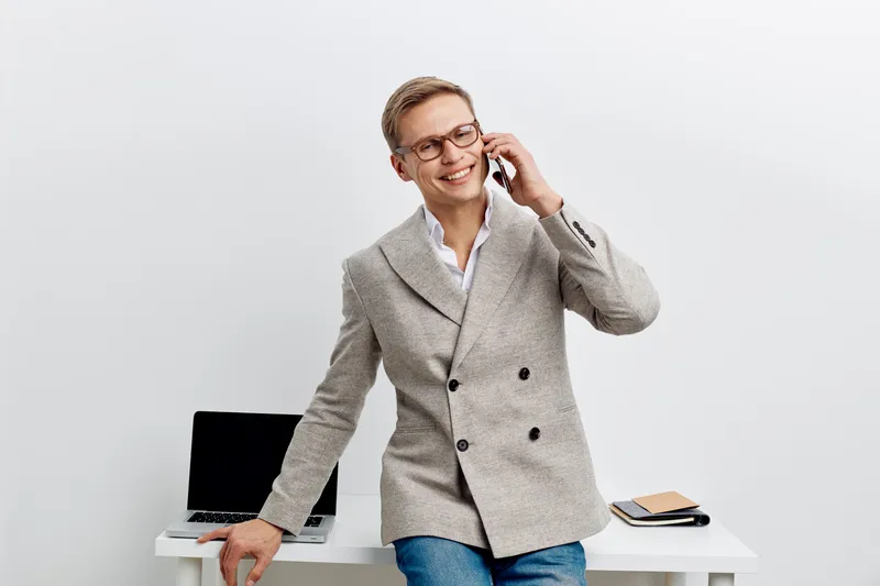 Confident smiling woman professional business attire talking on phone in office space with modern desk and computer workspace background. Modern corporate lifestyle concept