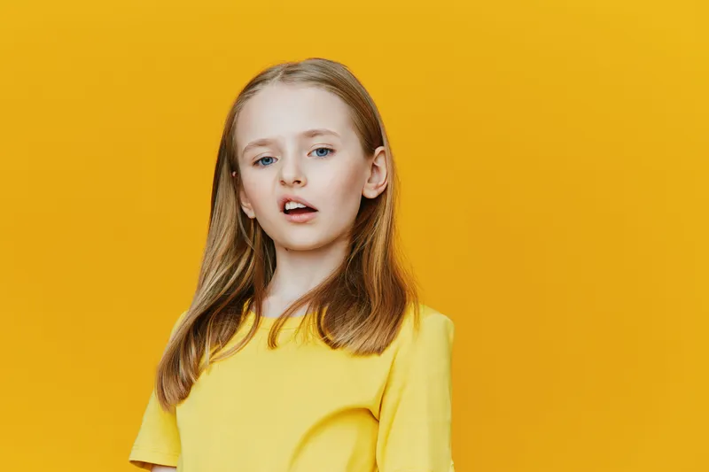 Young girl with long hair in a bright yellow shirt against a vibrant yellow background, expressing confidence and joy, perfect for youth fashion and positivity themes