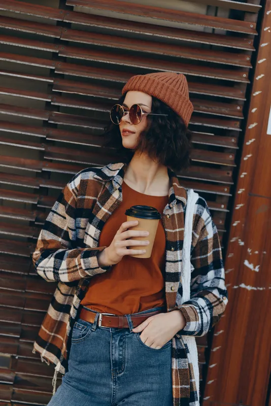 woman coffee street autumn casual beanie: candid lifestyle portrait of a young woman holding takeaway coffee on urban street, cozy plaid layers, golden hour glow, authenticity, mindful living,