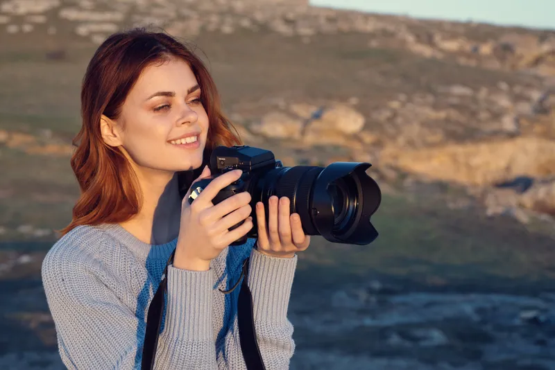 Жизнерадостная женщина-фотограф работает на открытом воздухе, среди природы, сочетая работу и образ жизни