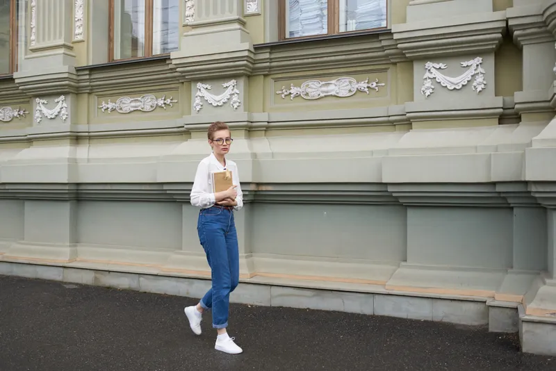 Симпатичная женщина в очках гуляет по городу с книгой, занимаясь образованием