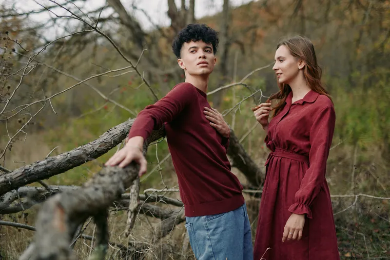 Young couple in an autumn meadow pose naturally beside a fallen tree, conveying quiet intimacy and a genuine connection that highlights authenticity and credibility in a candid lifestyle portrait.