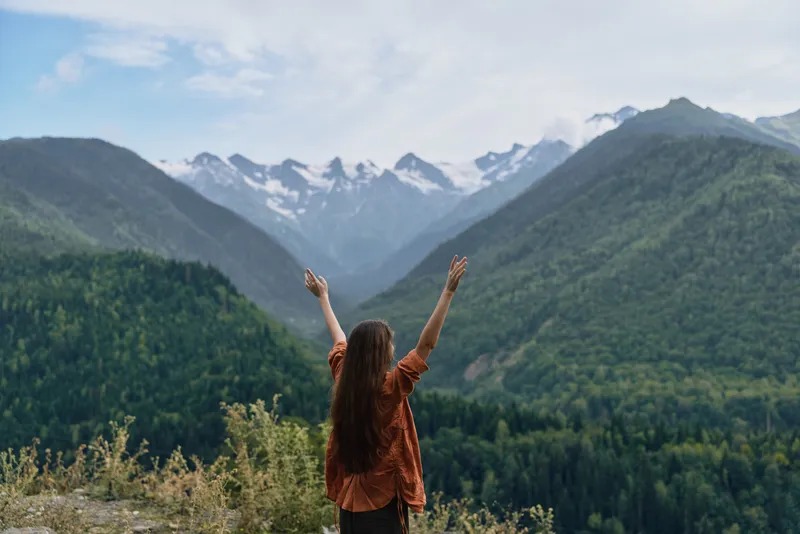 Person standing with arms raised admiring nature and landscape among mountains outdoors, expressing freedom and joy in the vast scenery and sky