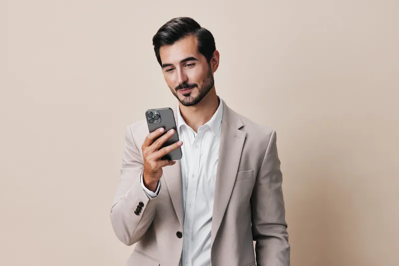 Улыбающийся мужчина в деловом костюме держит смартфон, сидя в помещении