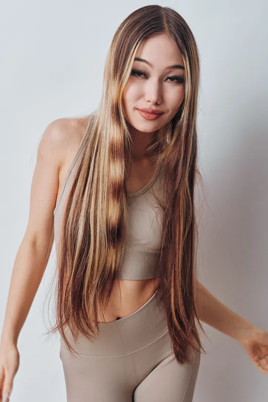 Young woman with long hair wearing beige sportswear posing against white background. Fitness, beauty and healthy lifestyle concept with natural makeup and casual posture indoors.