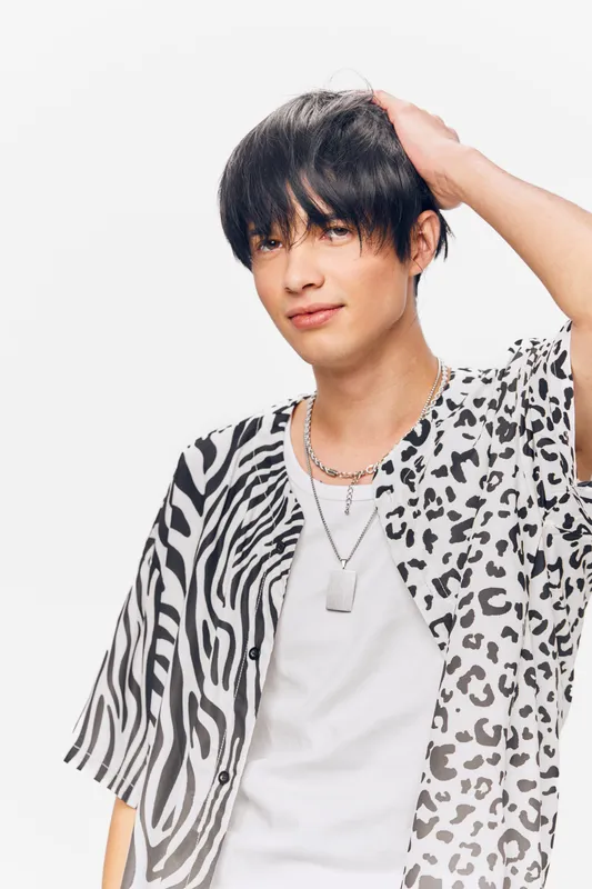 young man with short black hair wearing black and white animal print shirt, casual style, posing with hand on head against white background, trendy look