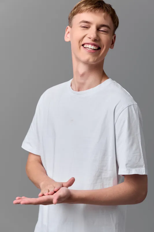 Smiling young man in a white t shirt gestures with open hands, casual pose conveying friendly vibe and positive energy for lifestyle and marketing visuals