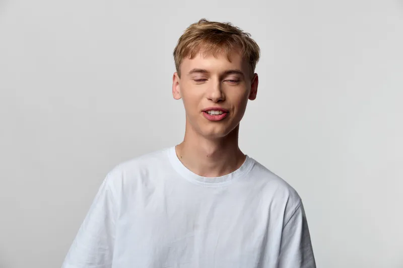 Young man in a white shirt with a relaxed smile in a clean studio, casual look, soft lighting and simple background capturing a fresh lifestyle moment suitable for fashion, wellness or social media