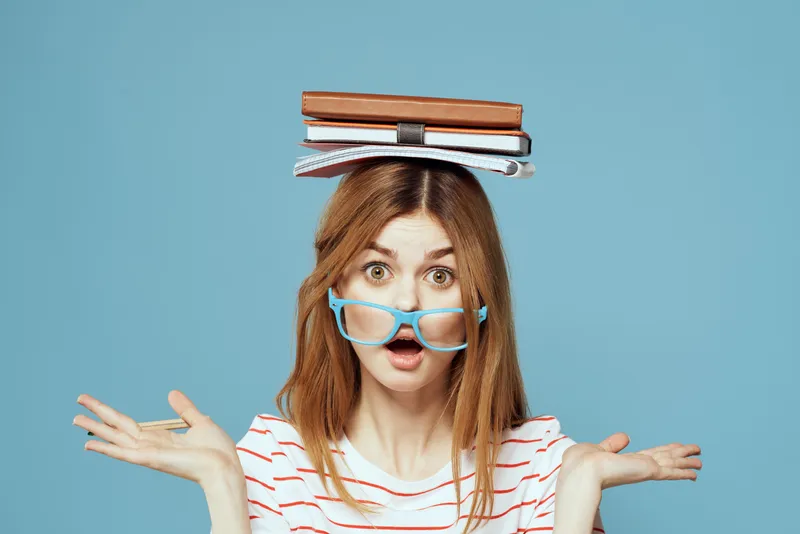 Студентка с книгами на голове, наука, образование, синий фон, эмоции, жестикуляция руками