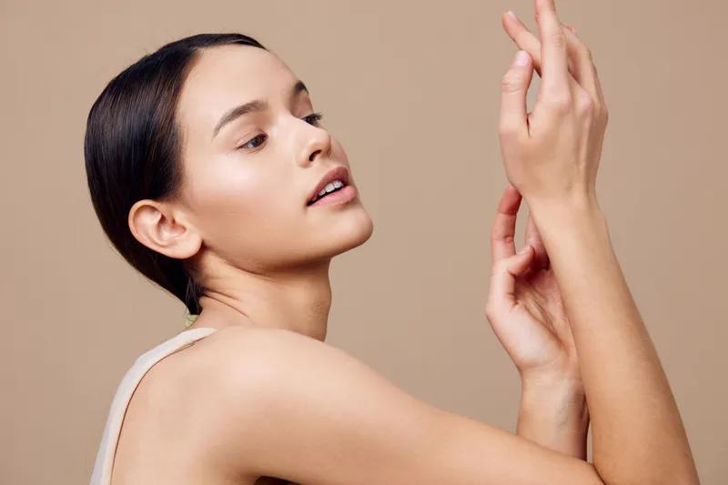 Elegant young woman showcasing natural beauty with a soft expression, neutral tone background highlighting skin care and wellness concepts