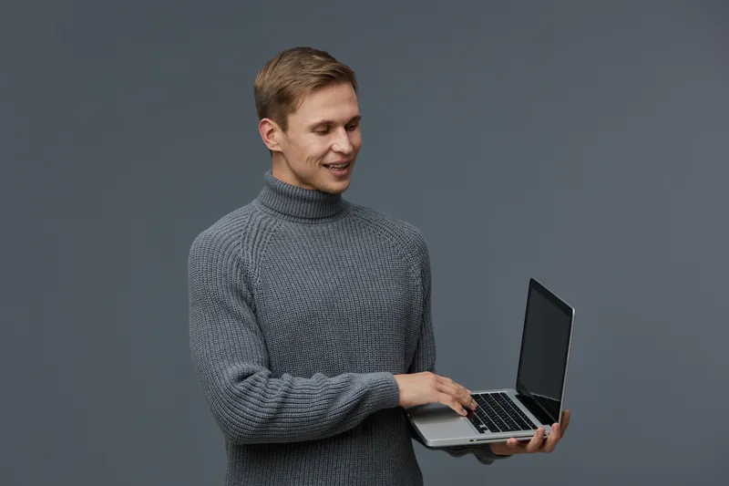 young caucasian man smiling gray turtleneck sweater hold laptop work digital nomad technology concept isolated gray background