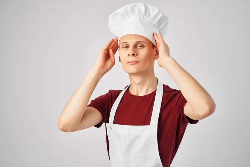 Мужчина в белом фартуке и колпаке на голове, рабочая униформа на кухне