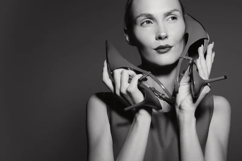 Portrait of a fair skinned white woman holding shoes near her face in black and white photo. Concept of fashion, beauty, and style with elegant expression.