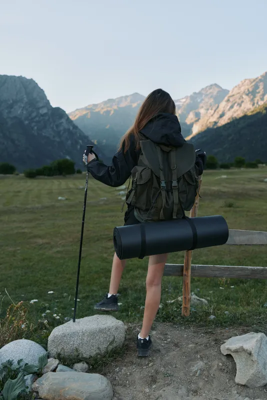 A solo hiker stands at a trailhead overlooking rugged mountains, wearing a backpack and trekking pole, ready for adventure and discovery.