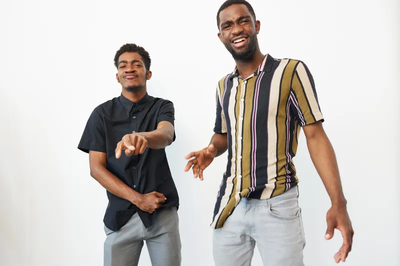 Two joyful African American men laughing together, showcasing happiness and friendship in a bright, minimalistic studio setting, perfect for creative projects.