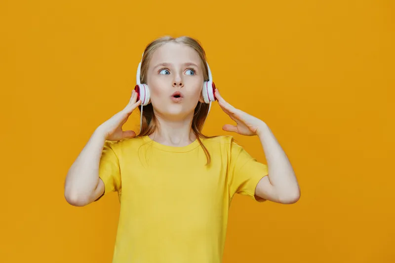 A cheerful girl listening to music with headphones, expressing joy against a bright yellow background, perfect for vibrant lifestyle concepts and music themes