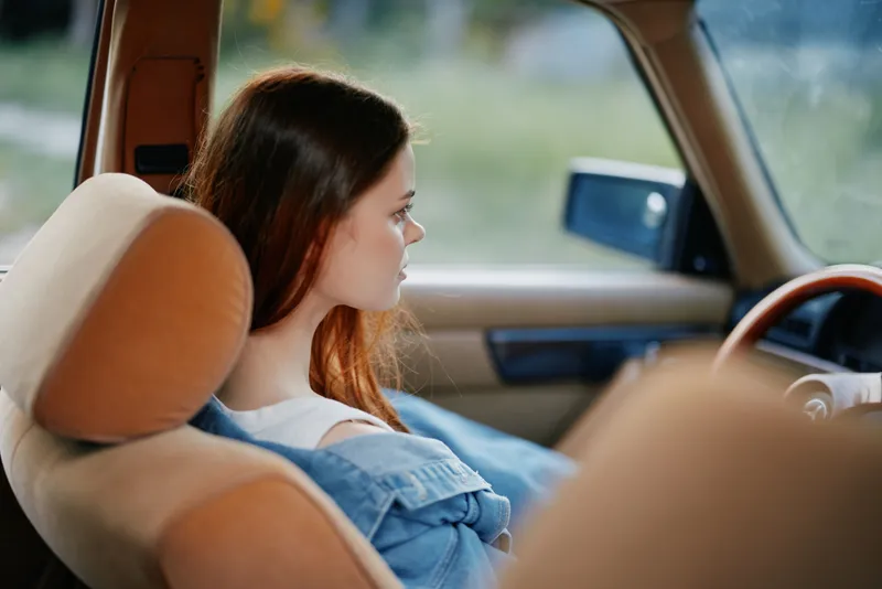 A young woman in casual attire, seated in a vintage car, reflecting on her journey with a serene expression, capturing the essence of nostalgia and adventure.