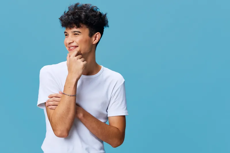 smiling man in white t-shirt poses against blue background, casual style, curly hair, youthful, happy expression, studio portrait, light mood