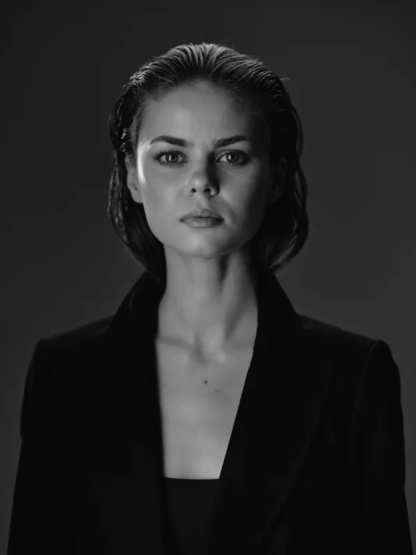 Black and white portrait of a serious woman with wet hair wearing a blazer, showing strength and confidence in a minimalistic setting.