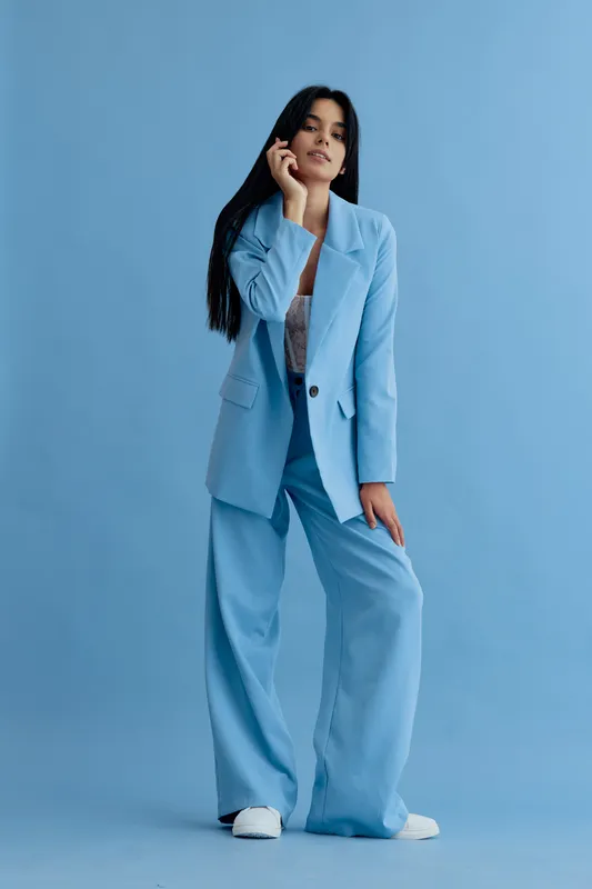Woman in blue pantsuit posing confidently against blue background, showcasing modern style and professional fashion with relaxed posture and natural expression.