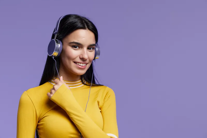 young woman sport fitness wearing yellow long sleeve top and headphones, smiling with dark straight hair and purple background, casual and active lifestyle concept