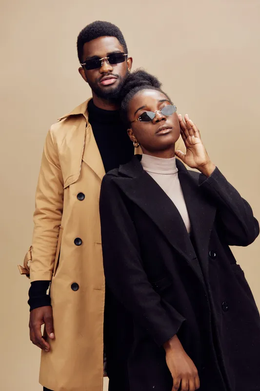 Fashionable young couple posing together, wearing stylish sunglasses and monochromatic outfits on a neutral background, showcasing modern urban style and confidence