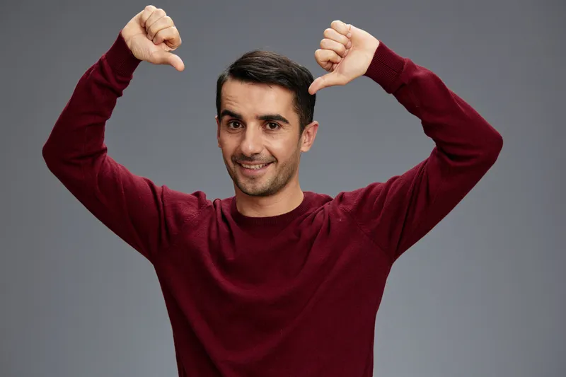 Мужчина в свитере показывает большой палец вниз, позирует с жестом руки, эмоции