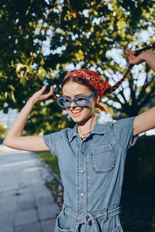 smiling woman in modern boho-western denim street style wearing blue sunglasses and red bandana with film color outdoor background in warm sunlight