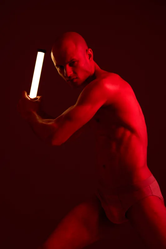 A striking man posing with a light in a dark red setting, showcasing strength and determination. The contrast emphasizes the artistic silhouette and dynamic movement.