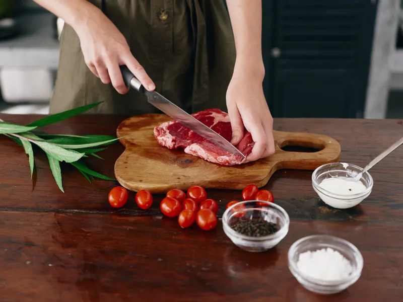 Женщина с ножом в руке режет стейк из мяса для жарки на кухне