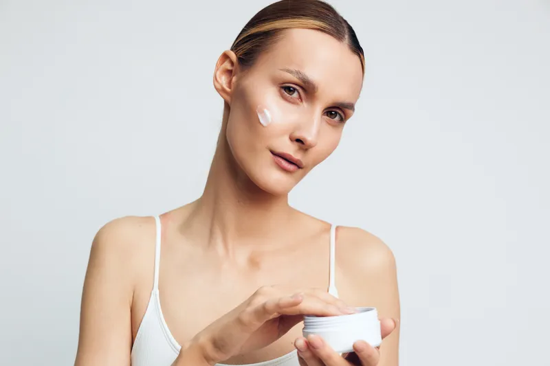 Woman skincare face cream jar beauty portrait studio wellness wellbeing, young woman holds white jar and applies moisturizer in close up soft light on clean background for calm routine