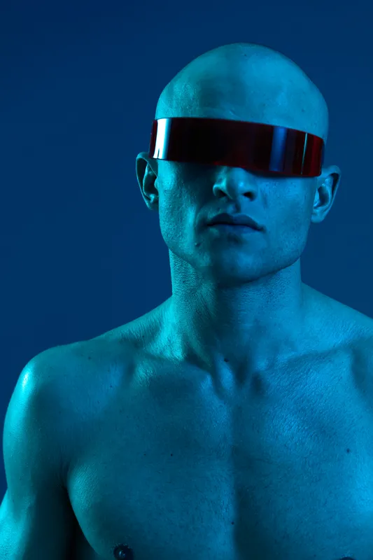 Portrait of a futuristic man wearing sleek red sunglasses, showcasing a striking blue color palette, emphasizing a bold and modern aesthetic in a black and white environment.