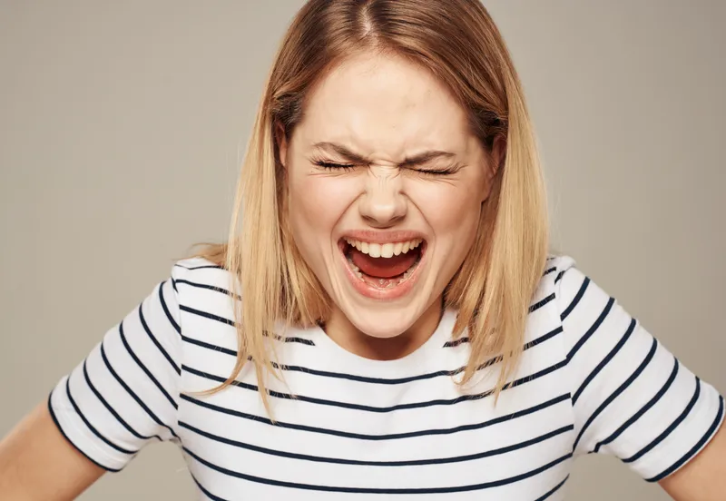Нервная женщина в полосатой футболке, блондинка, бежевый фон, крупный план портрета