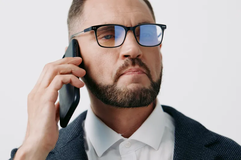 A focused business professional man on a colored isolated background speaks on a mobile phone with a confident, composed expression, exuding readiness and leadership.