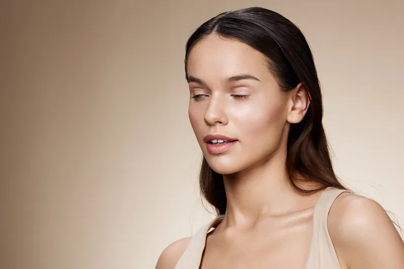 Portrait of a serene young model with long hair, wearing a natural tone outfit, conveying calmness against a soft beige background, emphasizing beauty and elegance