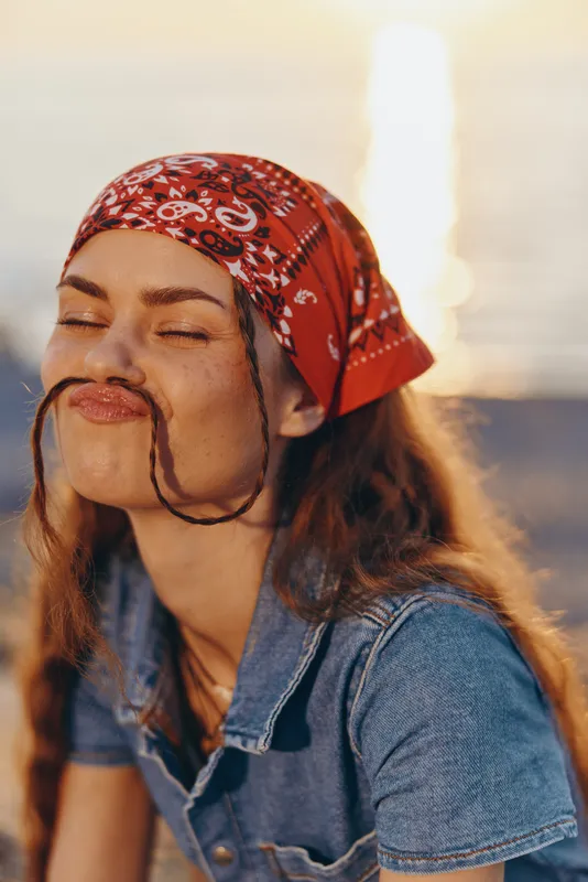 Lifestyle woman in modern boho-western denim street style with a red bandana and playful expression captured in warm film color tones.